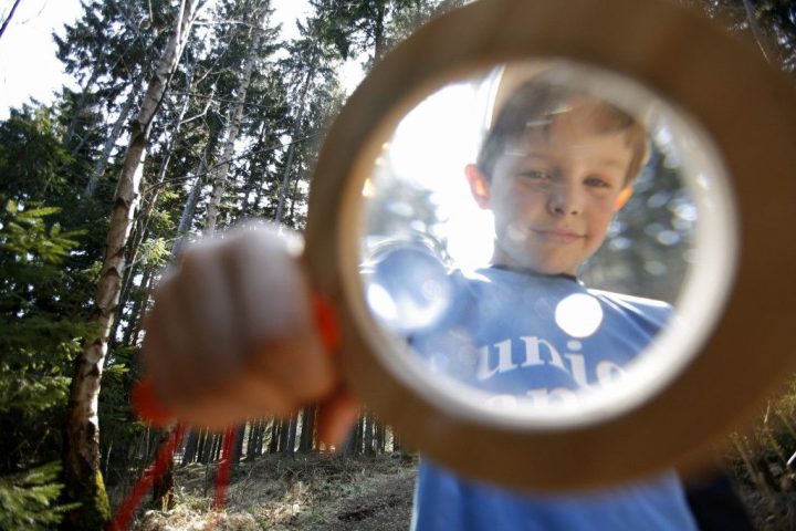 Ein Kind schaut im Wald durch eine Lupe