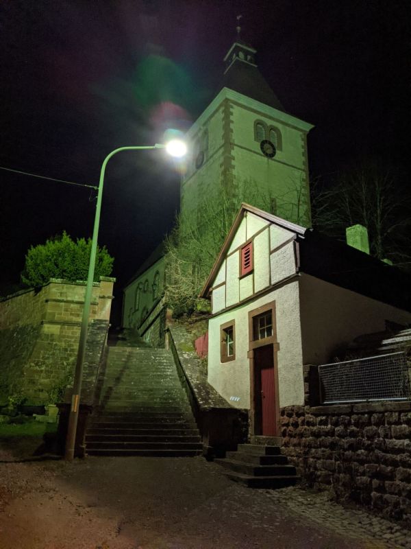 Die Nachtaufnahme zeigt die Straße vor der Rumbacher Kirche im Licht einer sternenfreundlichen Straßenlampe.