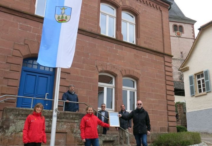 Mehrere Personen stehen vor dem Rathaus in Rumbach und freuen sich über die Übergabe des Zertifikats "Gemeinde unter den Sternen"