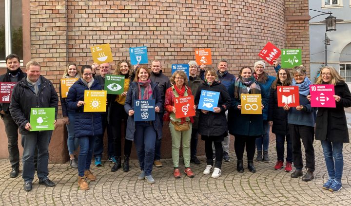 Das Bild zeigt die Teilnehmenden der erstn Steuerungsgruppensitzung der Stadt Speyer. Sie halten die Icons der Agenda 2030 in die Luft