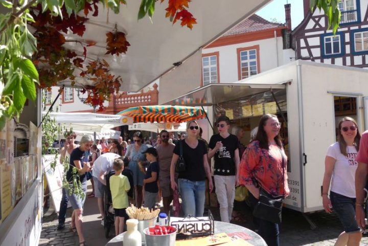 Das Bild zeigt Menschen, die an Marktständen vürübergehen.