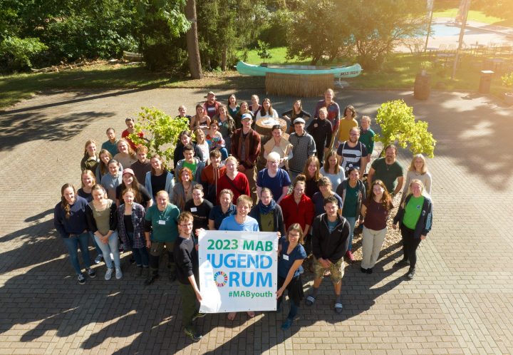 Es steht eine Gruppe Menschen zusammen auf einem Platz. Es wird ein Banner mit der Aufschrift "2023 MAB Jugendforum" hochgehalten.