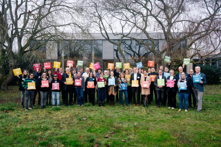 Das Bild zeigt eine Gruppe von Personen vor der Aula der Verwaltungsuniversität in Speyer. Die Personen halten jeweils eine buntes Schild mit einem der 17 Nachhaltigkeitsziele als Aufschrift.. 