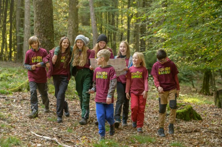 Kinder laufen gutgelaunt durch den Pfälzerwald. Sie tragen alle T-Shirts mit der Aufschrift "Junior Ranger"
