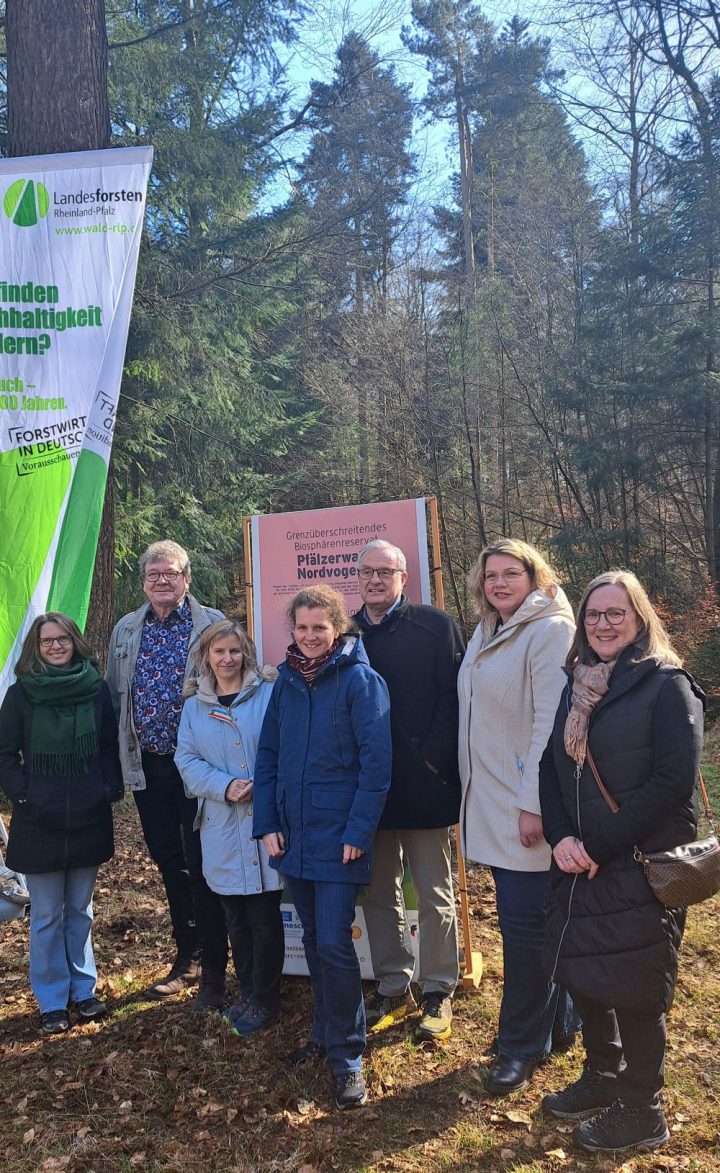 Auf dem Bild sieht man 7 Personen, die im Wald stehen. Hinter Ihnen sieht man eine Fahne von Landesforsten und einen Aufsteller des Biosphärenreservats Pfälzerwald.